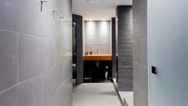 A modern bathroom with grey tiles, a wooden vanity, and a glass shower enclosure. - Hotel Kreuz by b_smart (Sachseln)