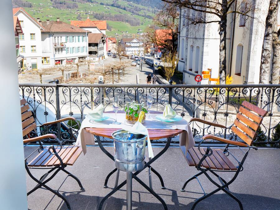 A balcony with a table set for two, featuring a metal bucket, wine glasses, and a flower arrangement.