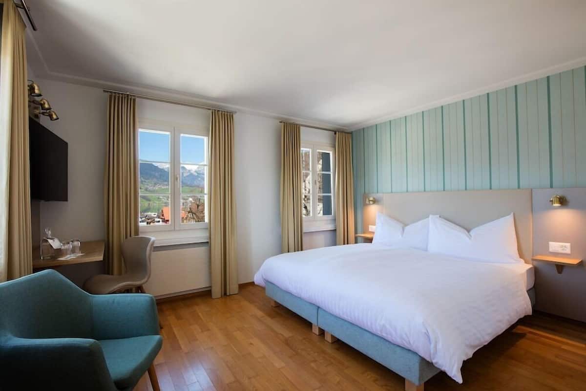 A hotel room with a bed, a chair, a desk, and a view of the mountains.