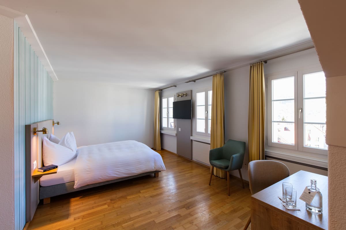 A hotel room with a bed, a desk, a chair, a TV, and a window with curtains.