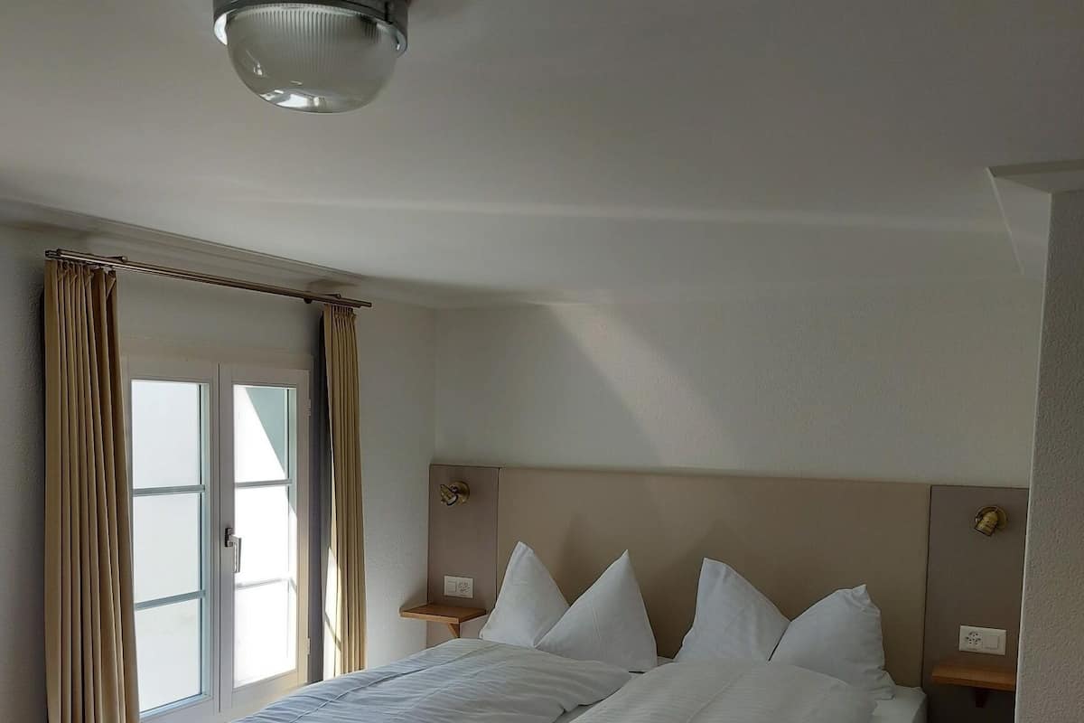 A hotel room with two beds, a window with curtains, a ceiling light, and a small bedside table.