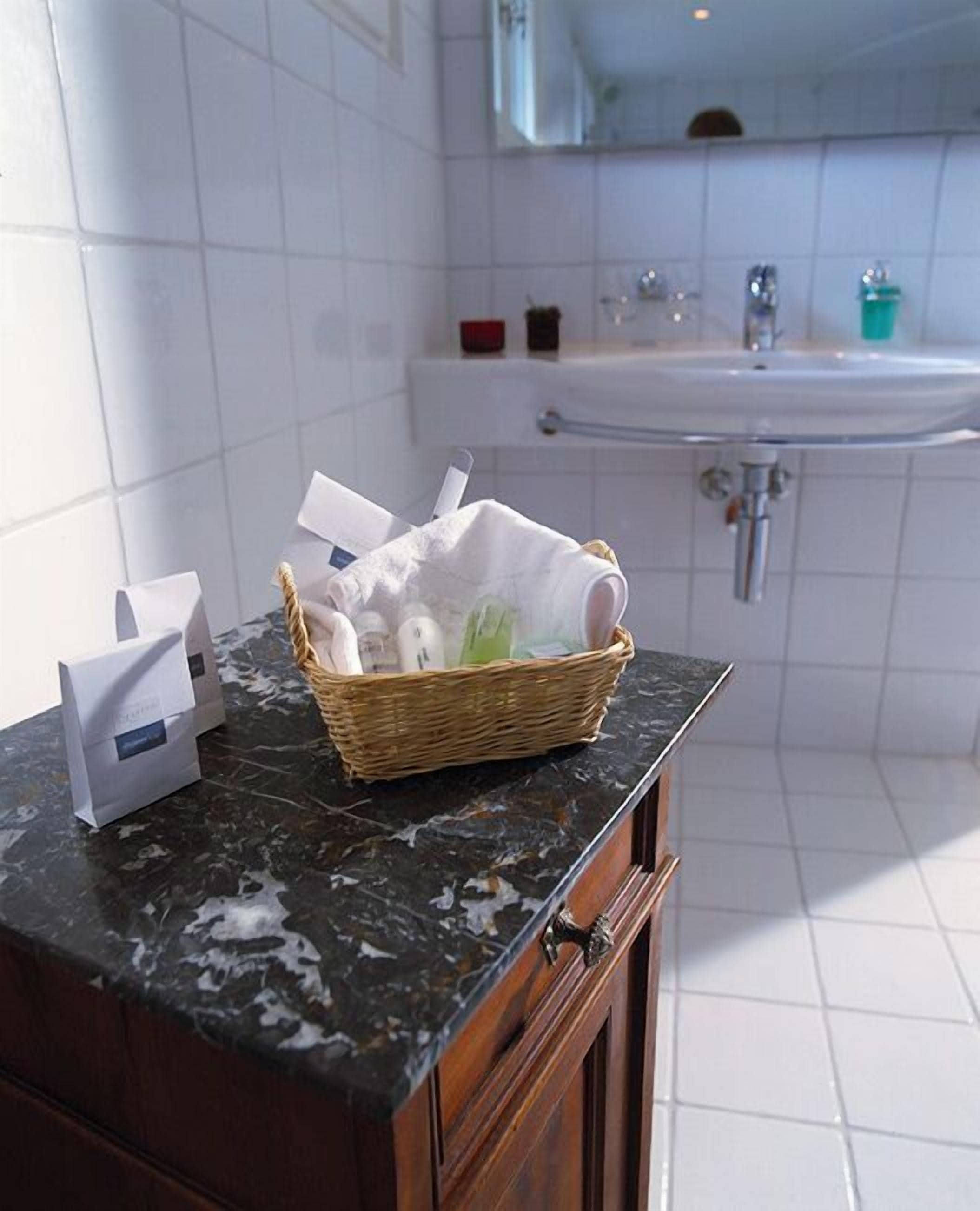 A bathroom with a marble countertop, a wicker basket with toiletries, a white towel, and a sink with a faucet.