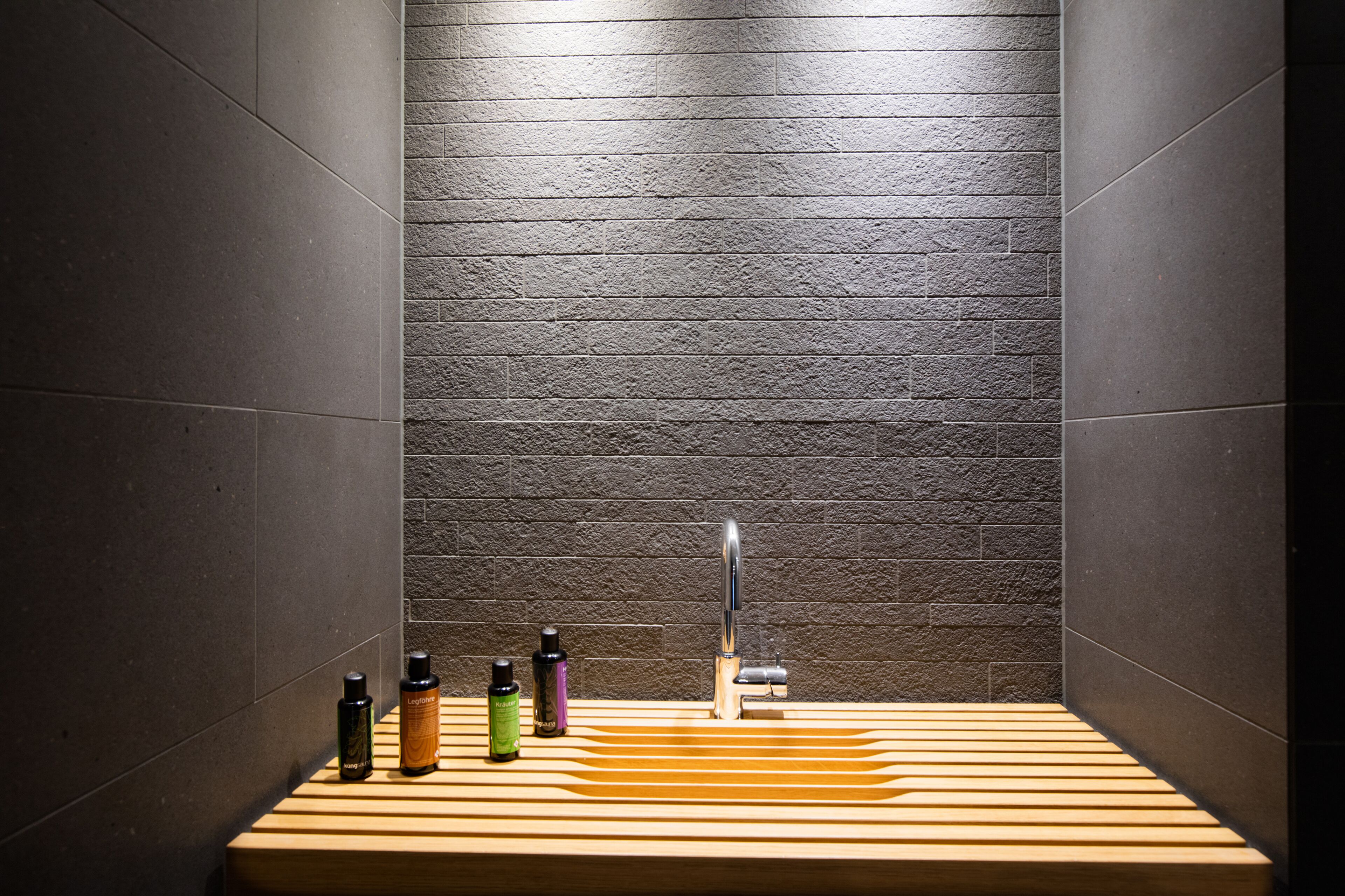 A bathroom with a wooden vanity, a modern faucet, and three bottles of toiletries.