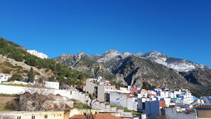 A coastal town with buildings on a hillside, a clear blue sky, and snow-capped mountains in the background. - Dar Al Machichi (Chefchaouen)