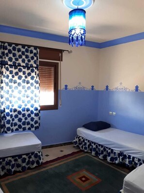 A room with two beds, a patterned curtain, a decorative ceiling light, and a window with blinds. - Dar Al Machichi (Chefchaouen)