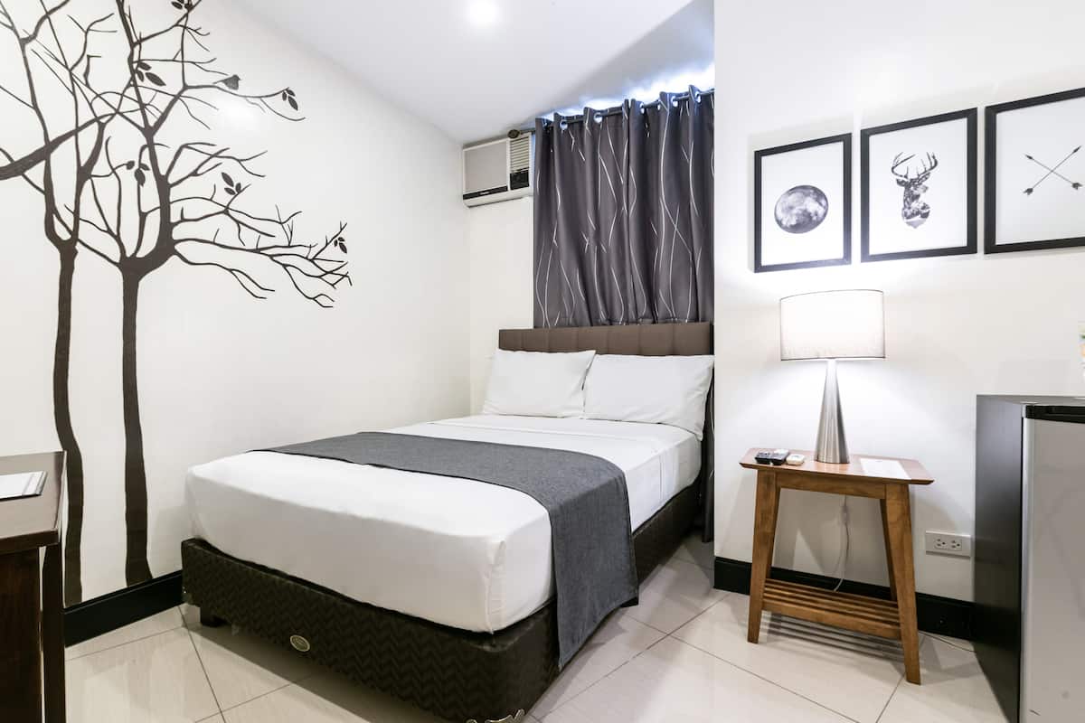 A modern hotel room with a bed, a bedside table with a lamp, and wall art.