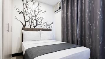 A neatly made bed with white and gray bedding, a tree mural on the wall, and a gray curtain with a wavy pattern.