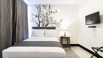 A hotel room with a bed, a nightstand, a lamp, a TV, and a wall art of a tree.