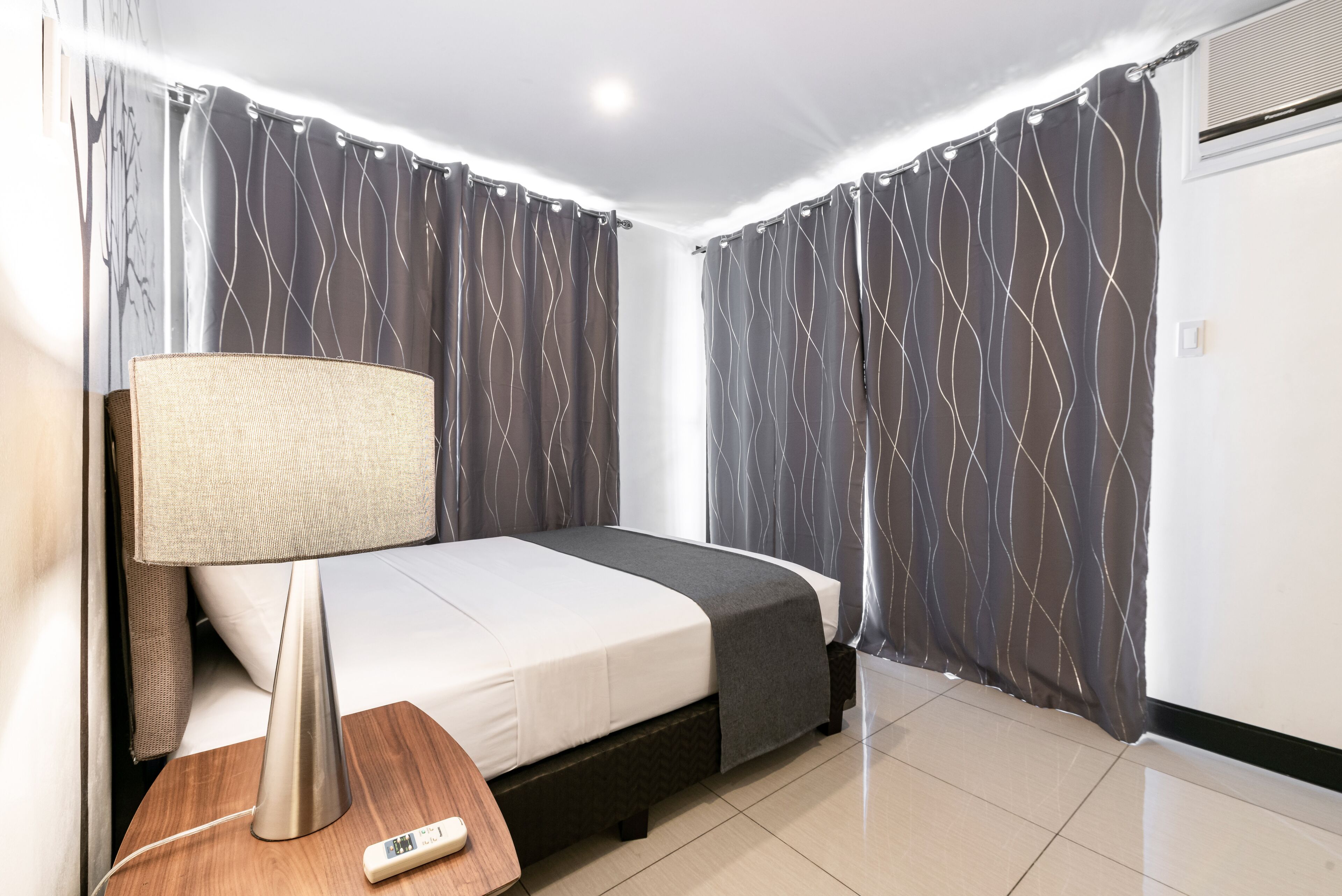 A hotel room with a bed, a bedside table with a lamp, and curtains.
