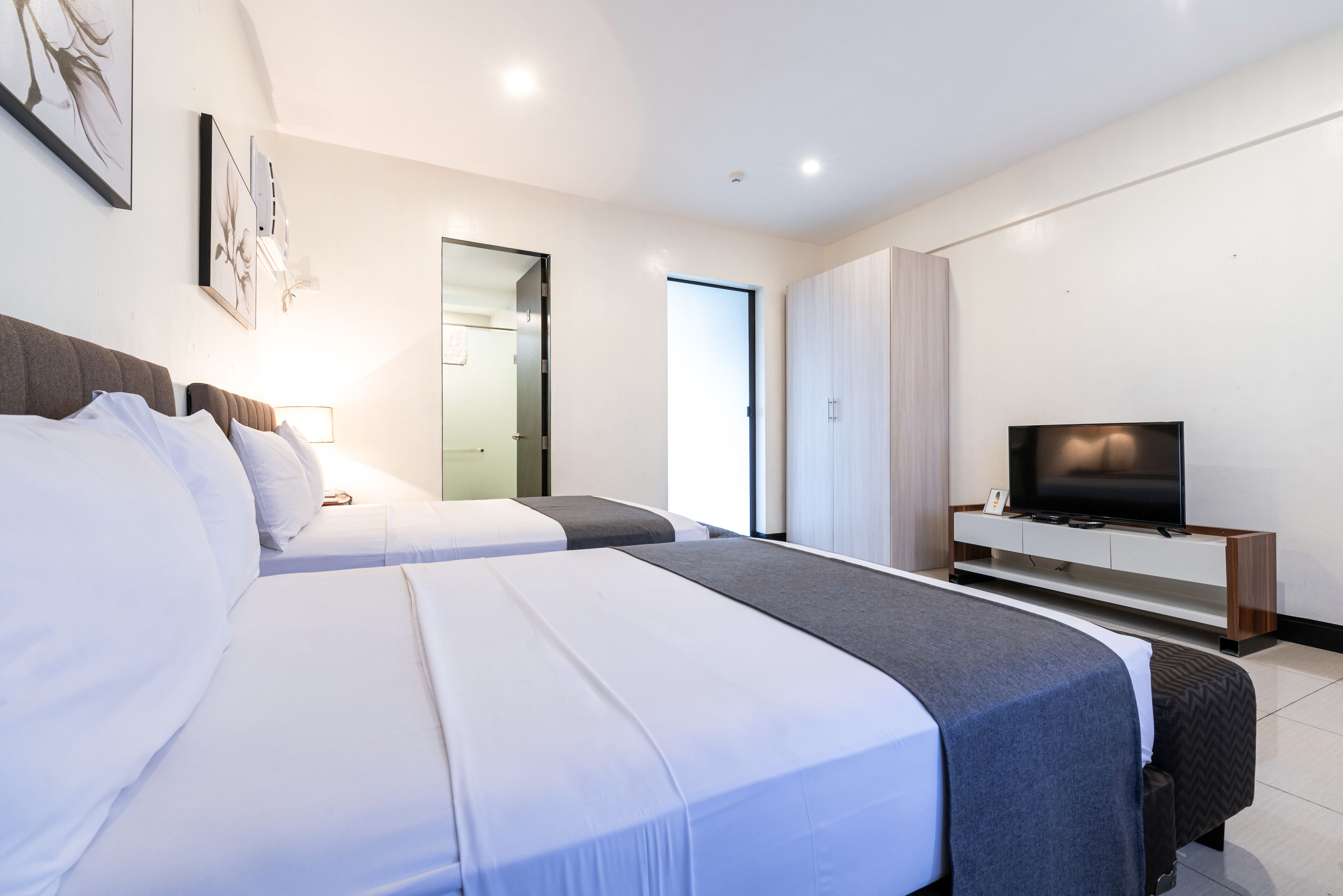 Habitació d'hotel moderna amb dos llits, un televisor i un armari.