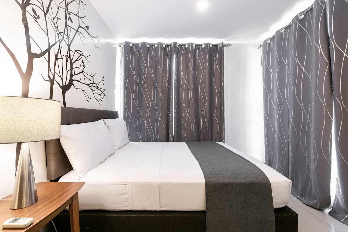 A neatly made bed with a white and gray bedspread, a bedside lamp, and a wall-mounted tree decal.