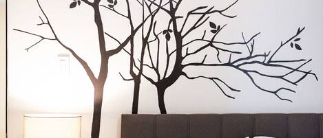 A bedroom with a bed, a nightstand, a lamp, and a wall decal of a tree with birds.