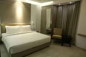 A hotel room with a large bed, a chair, a vanity with a mirror, and a curtain. - Keys Lite by Lemon Tree Hotels, Mayfield, Gurgaon (Gurugram)