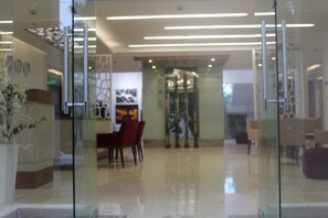 Un vestíbulo moderno con puertas de vidrio, una mesa de recepción y una zona de estar con sillas y una mesa.