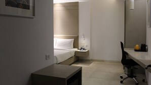 A hotel room with a bed, bedside table, desk, chair, and a small table. - Keys Lite by Lemon Tree Hotels, Mayfield, Gurgaon (Gurugram)