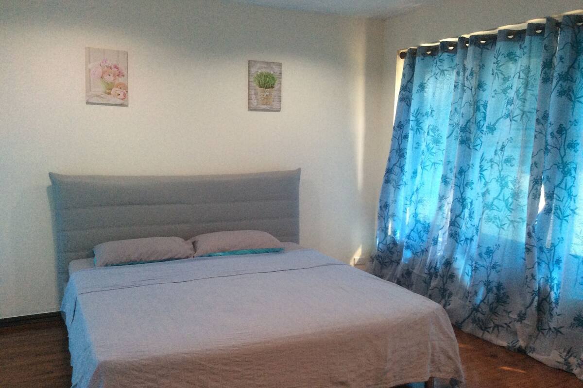 Une chambre à coucher avec un lit, une tête de lit et une fenêtre ornée de rideaux à motifs floraux.