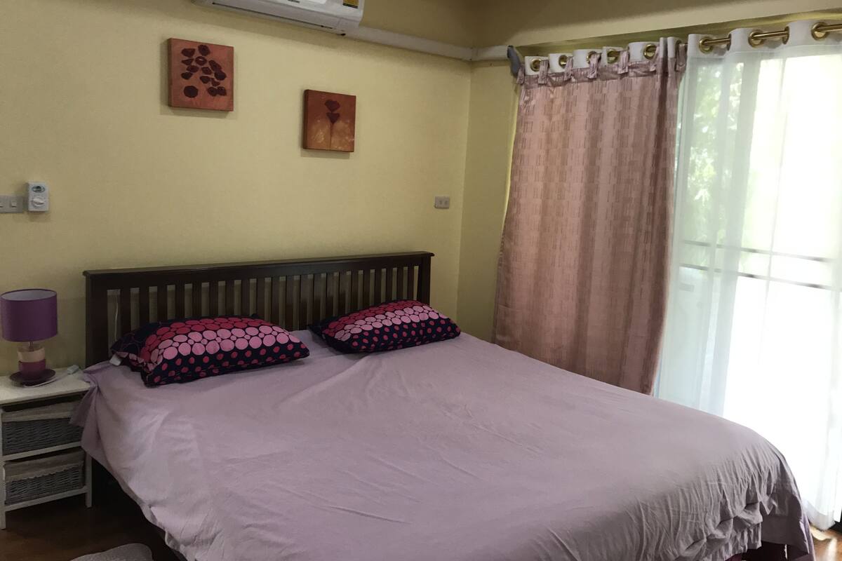 Une chambre à coucher avec un lit, une table de chevet, un climatiseur et une fenêtre avec des rideaux.