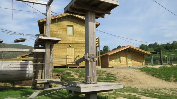 Una baita di legno con una piccola finestra e una porta, circondata da un'area recintata e un sentiero sterrato che vi conduce.