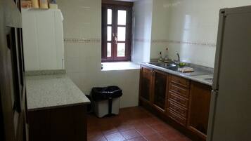 A kitchen with white cabinets, a window, a sink, and a trash bin.