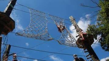 A person navigating a rope course with netted sections and wooden poles.