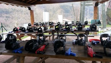 Katettu ulkoalue, jossa on useita piknikpöytiä ja esillä on paintball-varusteita ja -välineitä.