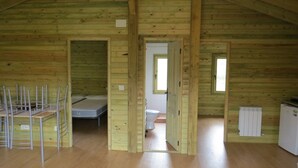 Interno di una baita in legno con letto a soppalco, bagno piccolo e angolo cottura.