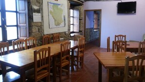 Un'area pranzo con tavoli e sedie in legno, una mappa appesa al muro e un televisore montato.