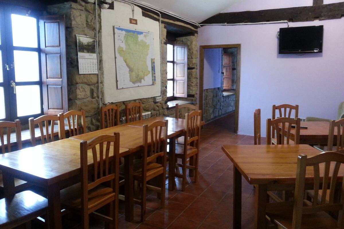 A dining area with wooden tables and chairs, a map on the wall, and a television mounted on the wall.