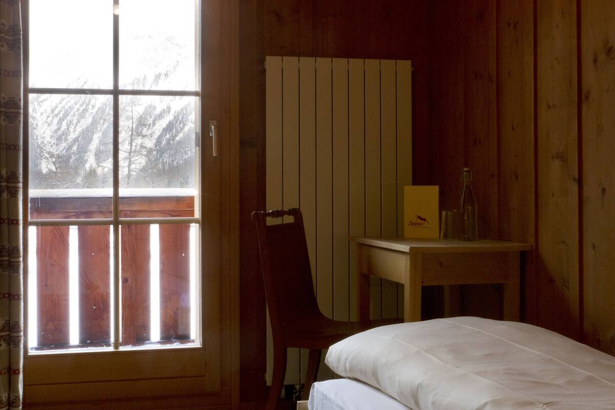 A wooden room with a bed, a small table, and a radiator.