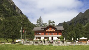 A wooden chalet with a balcony, surrounded by mountains and trees.