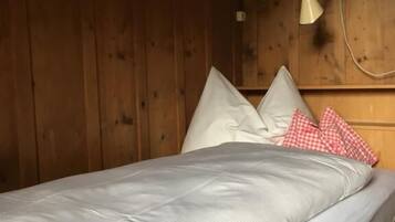 Un lit simple avec un matelas et des oreillers blancs, une tête de lit en bois et une lampe fixée au mur.