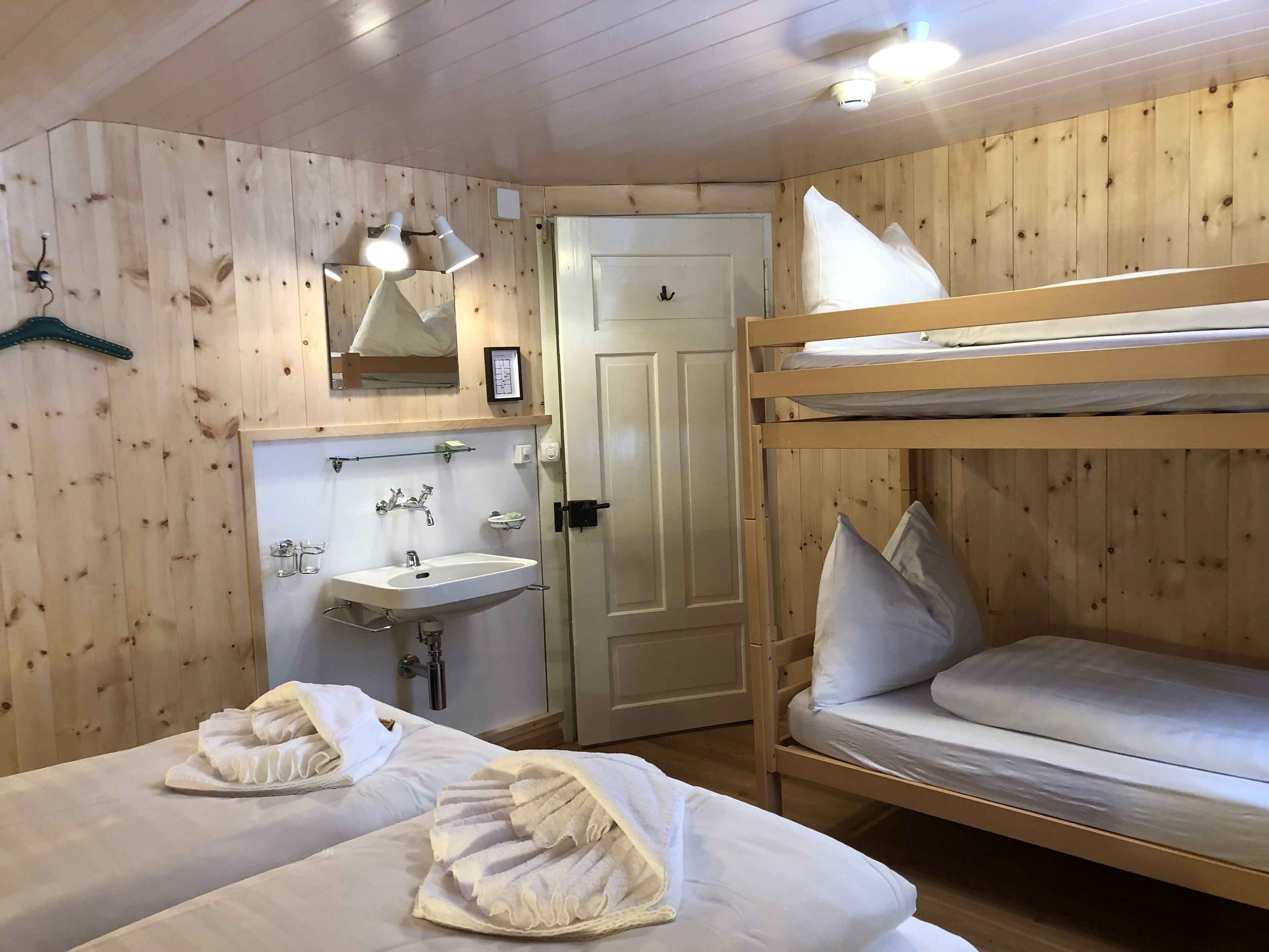 Una habitación tipo cabaña de madera con literas, un lavabo y un espejo.