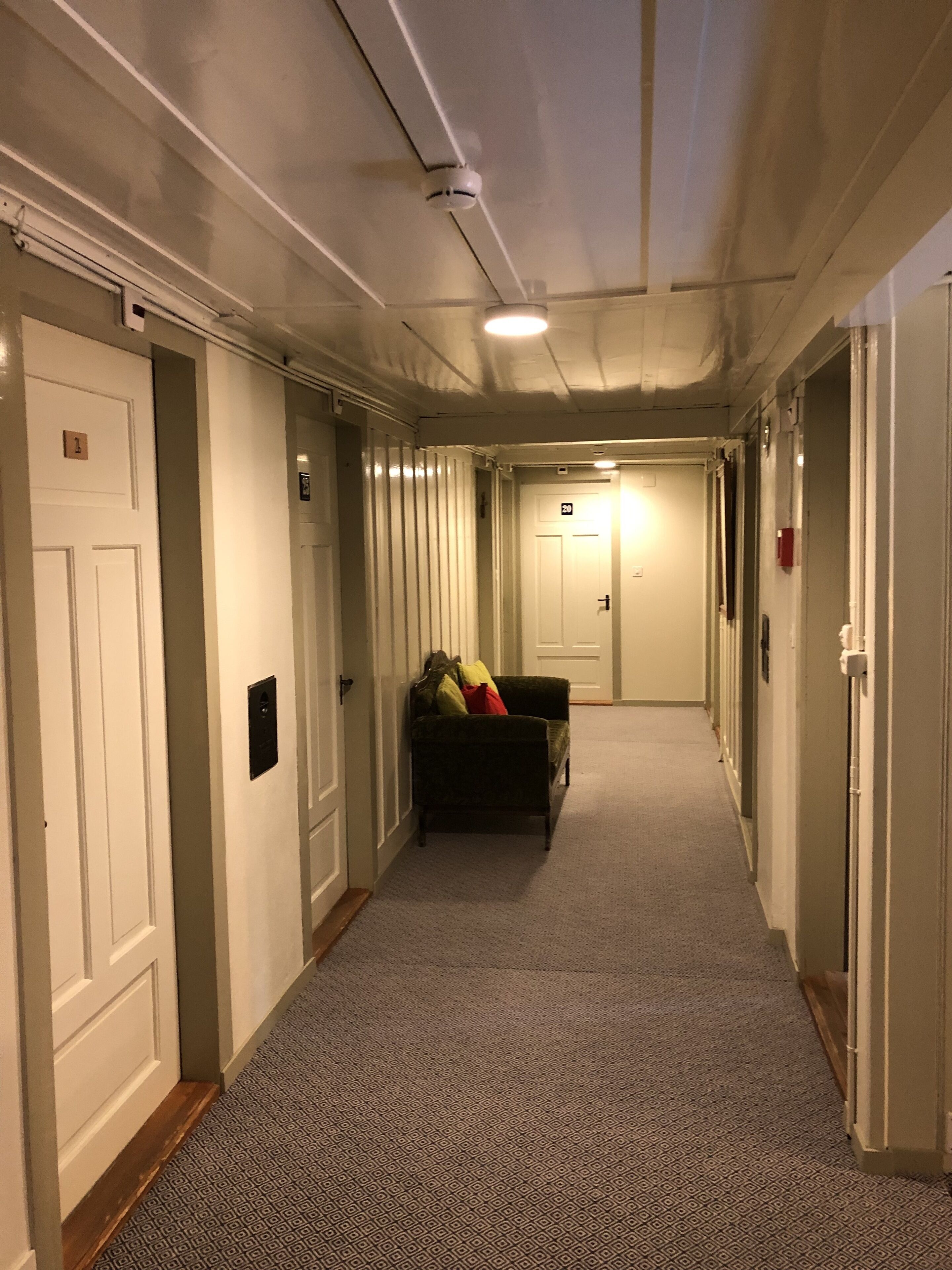 A hallway with carpeted floors, white doors, and a couch with pillows.