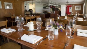 A restaurant with wooden tables set for dining, clear glassware, and a bar area in the background.