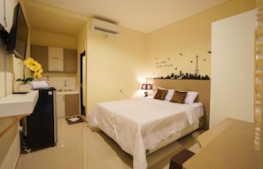 Ein Hotelzimmer mit Bett, Schreibtisch, einer kleinen Küchenzeile und einem Wandbild einer Stadtansicht.