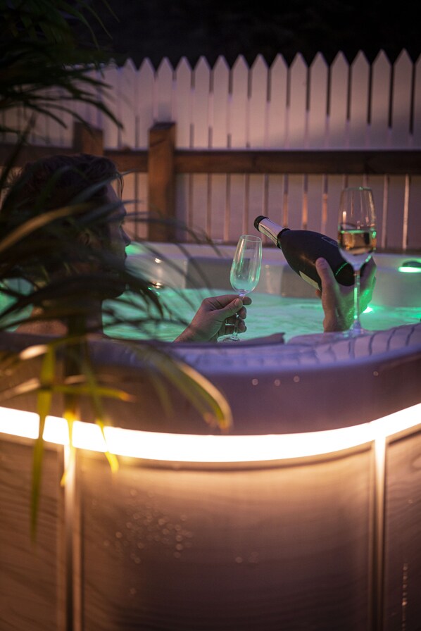 Una persona relajándose en un jacuzzi con una botella y un vaso.