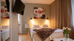 A hotel room with a bed, a TV mounted on the wall, and a painting above the bed. - Slottshotellet Annex (Kalmar)