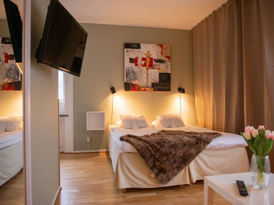 A hotel room with a bed, a TV mounted on the wall, and a painting above the bed.