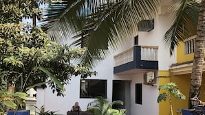 A courtyard with a palm tree, a potted plant, and a person sitting at a table. - Blue Marine Resort (Calangute)