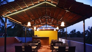 An outdoor restaurant with a covered seating area, a bar, and a view of palm trees. - Blue Marine Resort (Calangute)