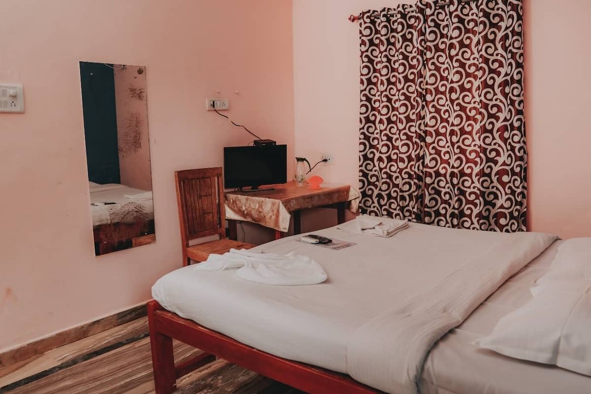 A bedroom with a bed, a desk with a computer, a mirror, and patterned curtains.