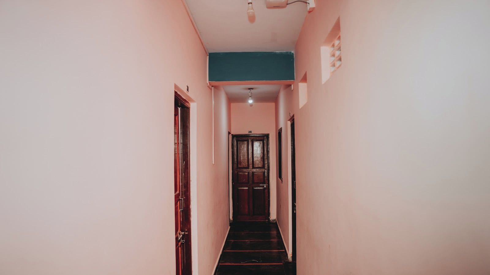 Un pasillo estrecho con una puerta de madera al final, una lámpara en el techo y el número '36' en la pared.