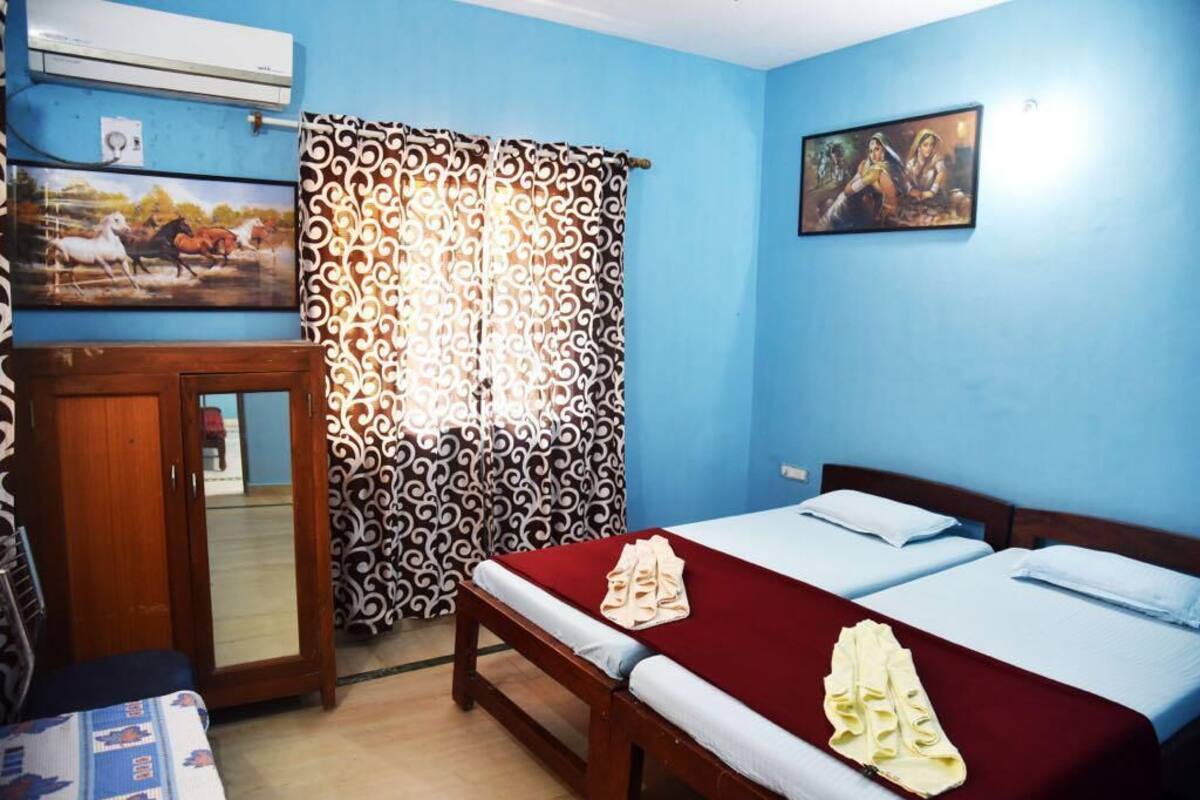 A room with two beds, a wooden cabinet, a patterned curtain, and two wall-mounted paintings.