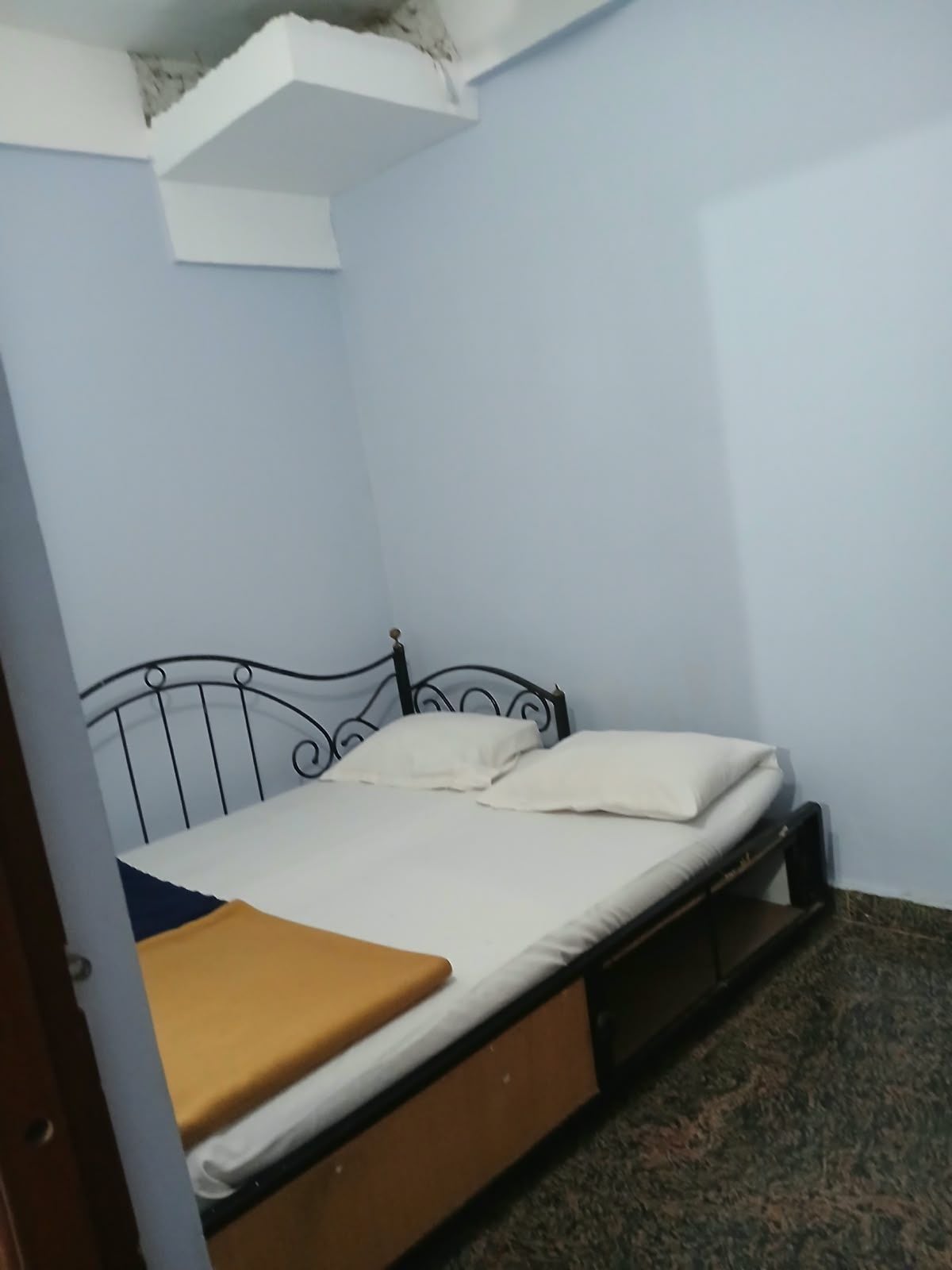 A single bed with a metal frame and white bedding in a room with light blue walls and a carpeted floor.
