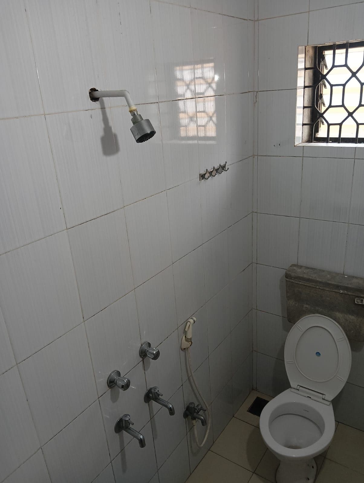 Un bagno piccolo rivestito di piastrelle, con il water, una doccetta e una finestra con una griglia metallica.