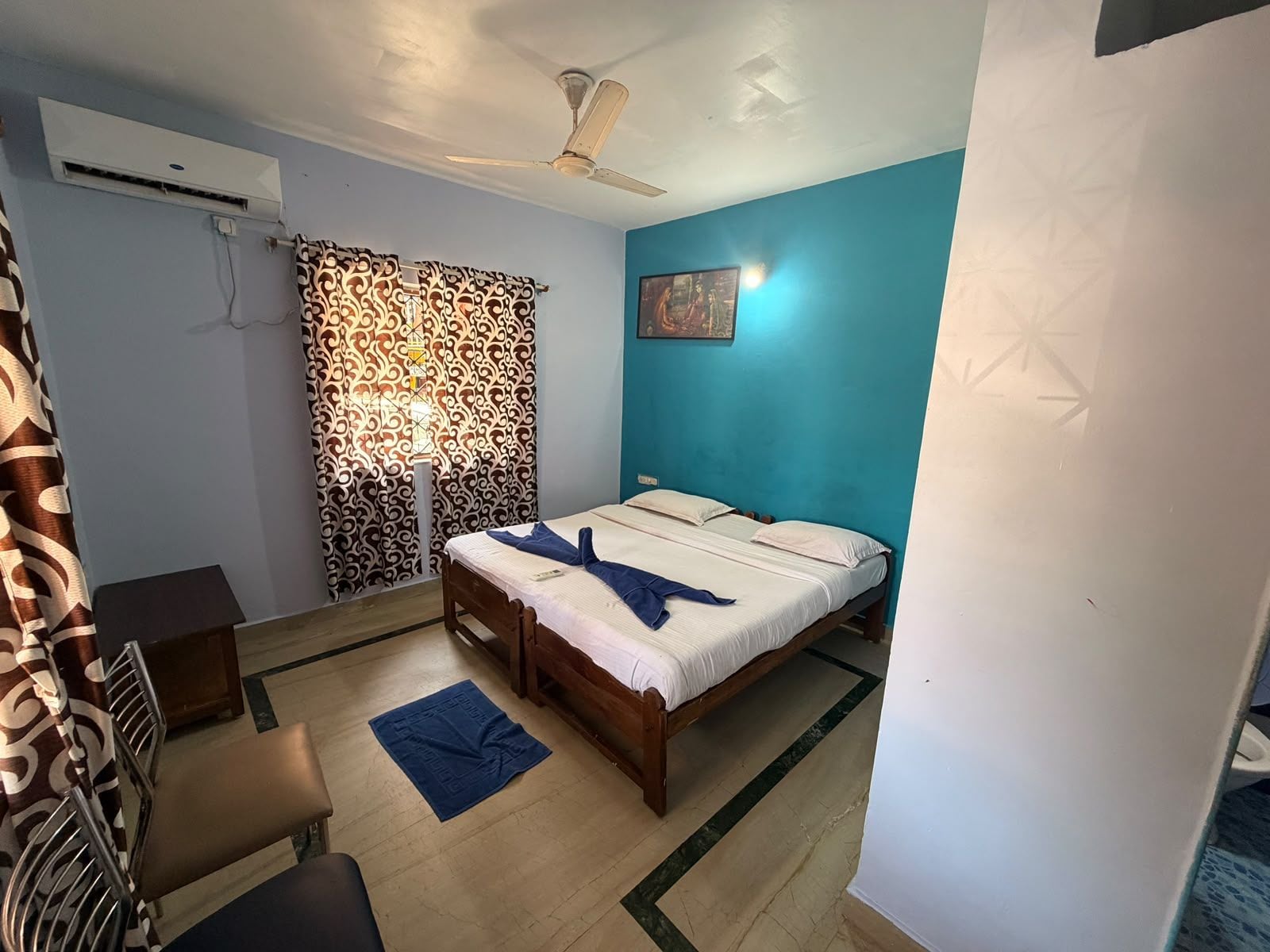 A bedroom with a bed, a ceiling fan, an air conditioning unit, a patterned curtain, and a blue rug.
