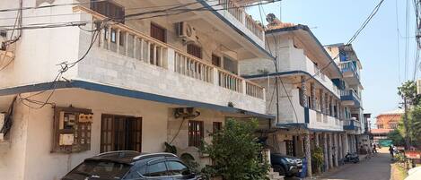 A multi-story residential building with balconies, parked cars, and a dog on the street.