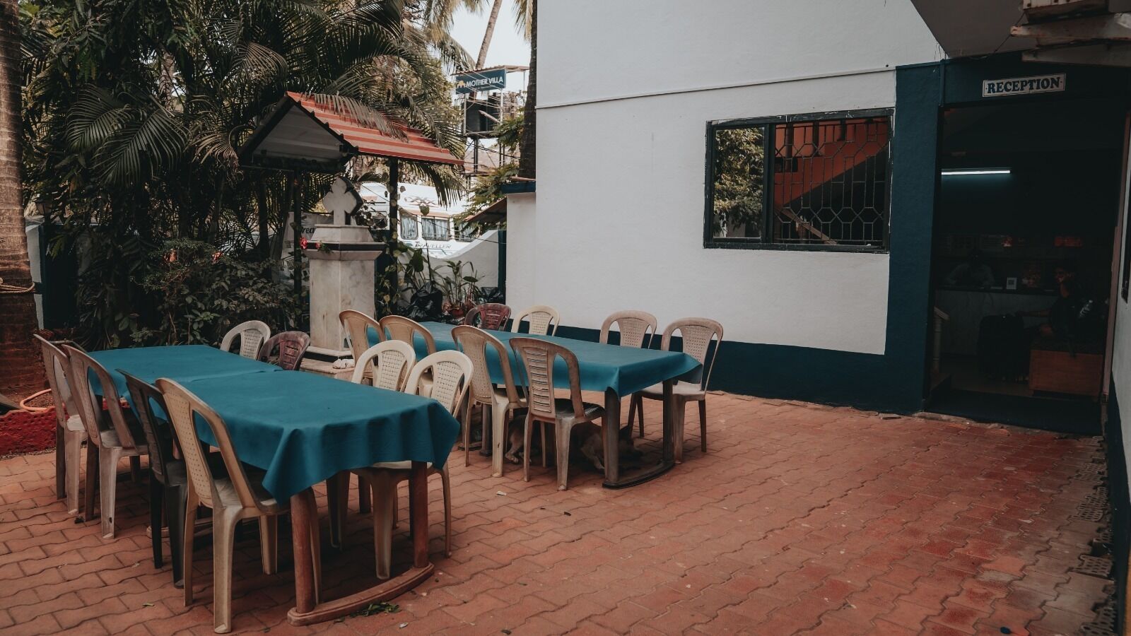 An outdoor dining area with tables and chairs, a reception area, and a building with a sign reading "MOTHERVILLA".