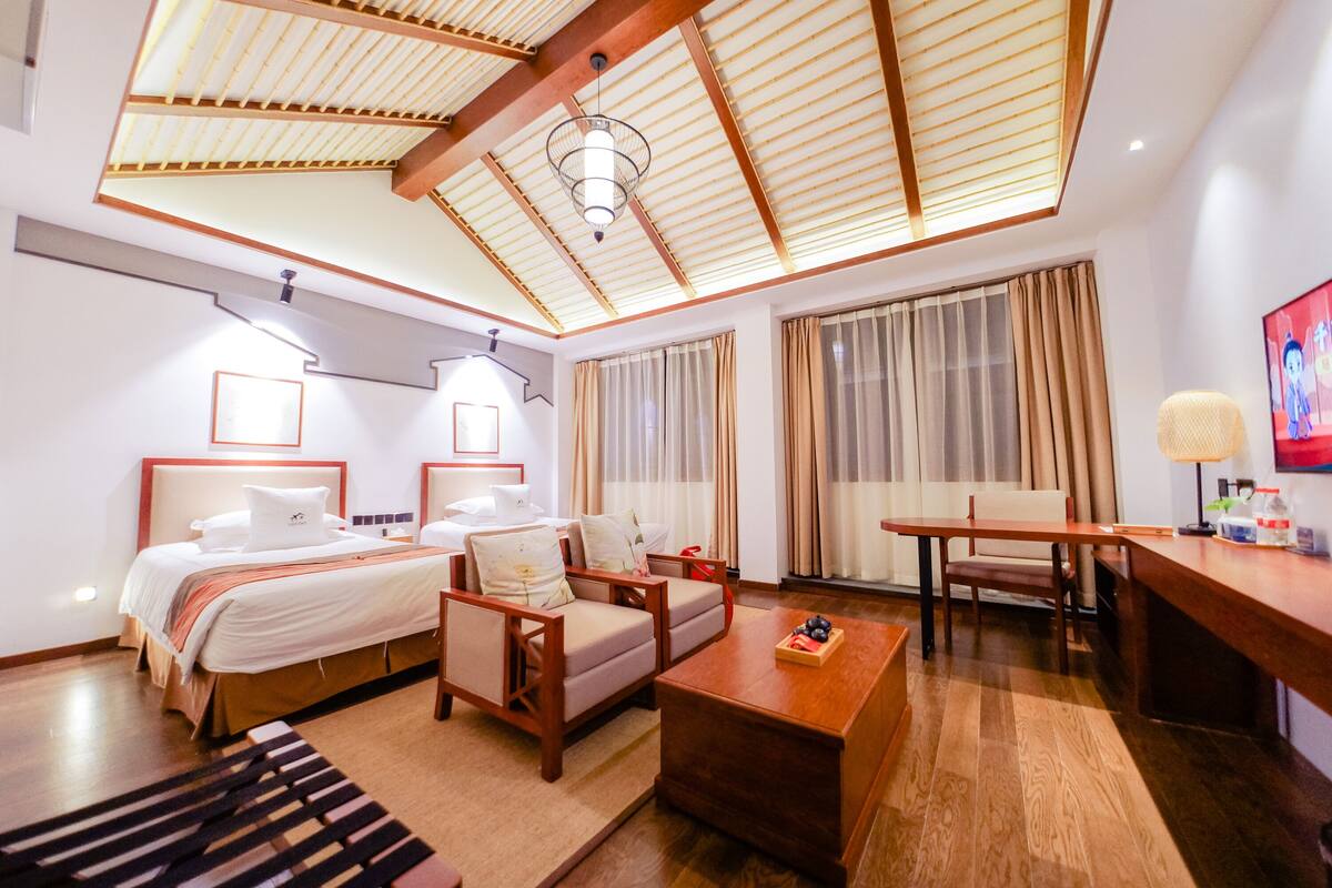 A hotel room with a bed, two chairs, a small table, a desk, and a ceiling fan.