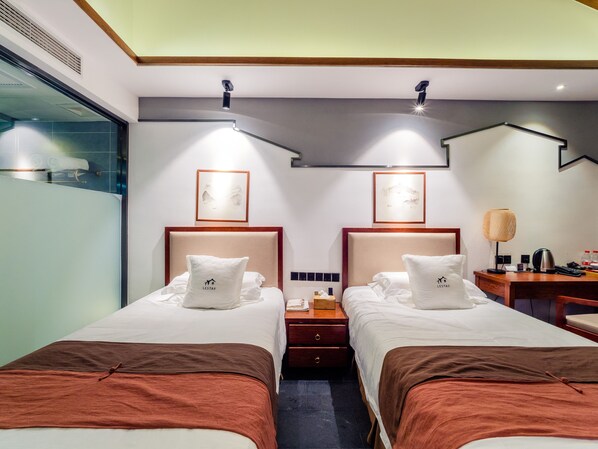 A hotel room with two beds, a nightstand, a lamp, and framed artwork on the wall. - CQJ Lestay Hotel (Hangzhou)